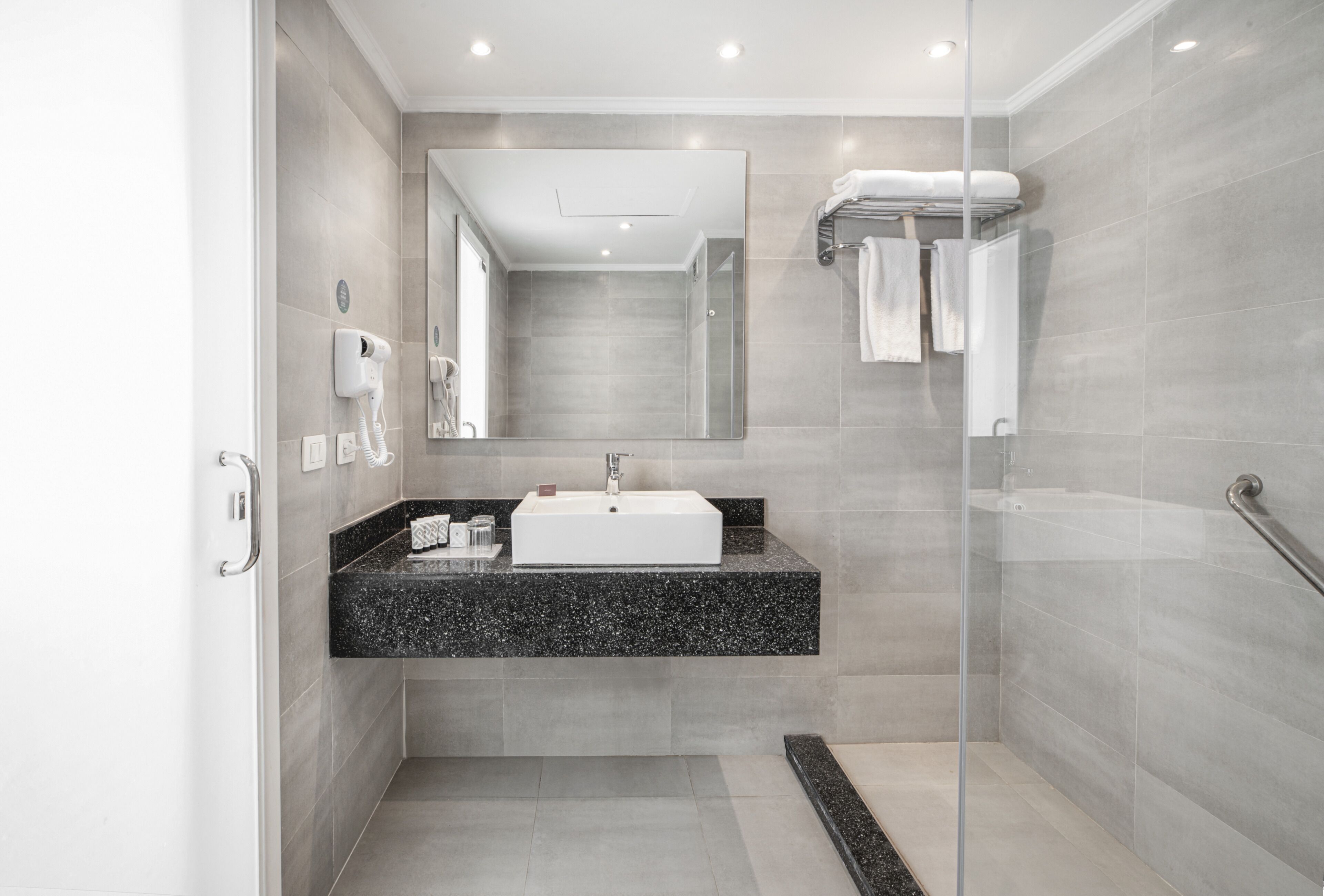 A modern bathroom with a glass shower enclosure, a white sink, and a black granite countertop.