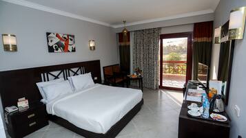 A hotel room with a large bed, a desk with a chair, a small table with a water bottle and a kettle, and a view of the outdoors through a sliding door.
