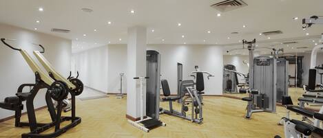 Une salle de sport équipée de divers appareils d’exercice, dotée d’un plancher en bois et d’un mur recouvert de miroirs.