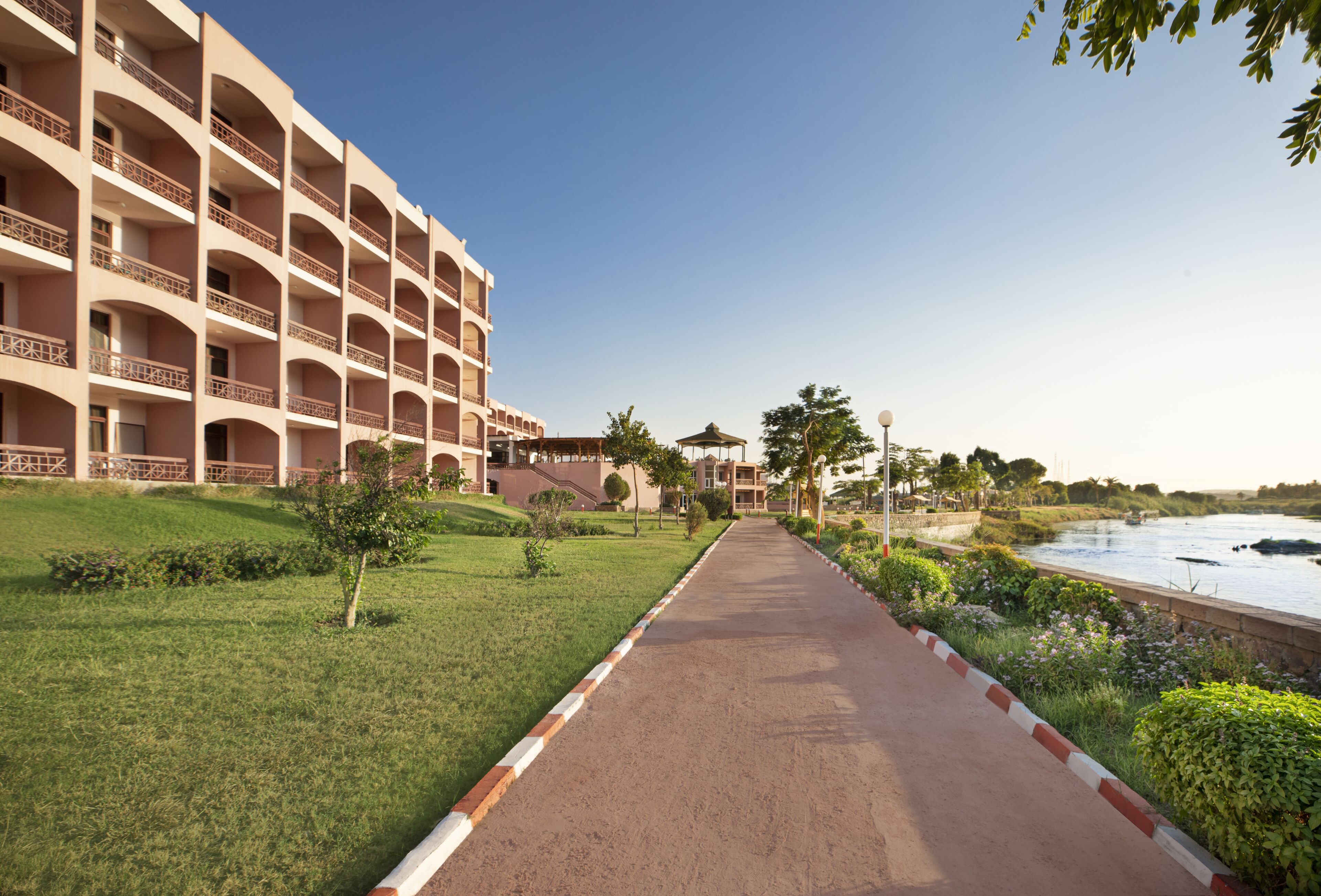 Un hotel con varios balcones, un camino que lleva a la playa y un cielo despejado.