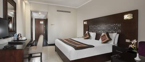 Habitación de hotel con cama, escritorio, silla, televisor y un panel decorativo en la pared.