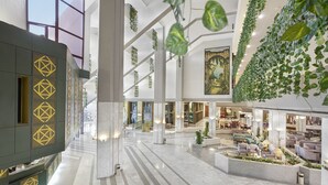 Un vestíbul ampli amb sòl de marbre, una zona de recepció amb motius geomètrics i una zona de seients amb plantes i mobles.