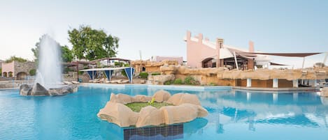 Una piscina con una fuente de agua, rodeada de formaciones rocosas y un edificio de diseño moderno.
