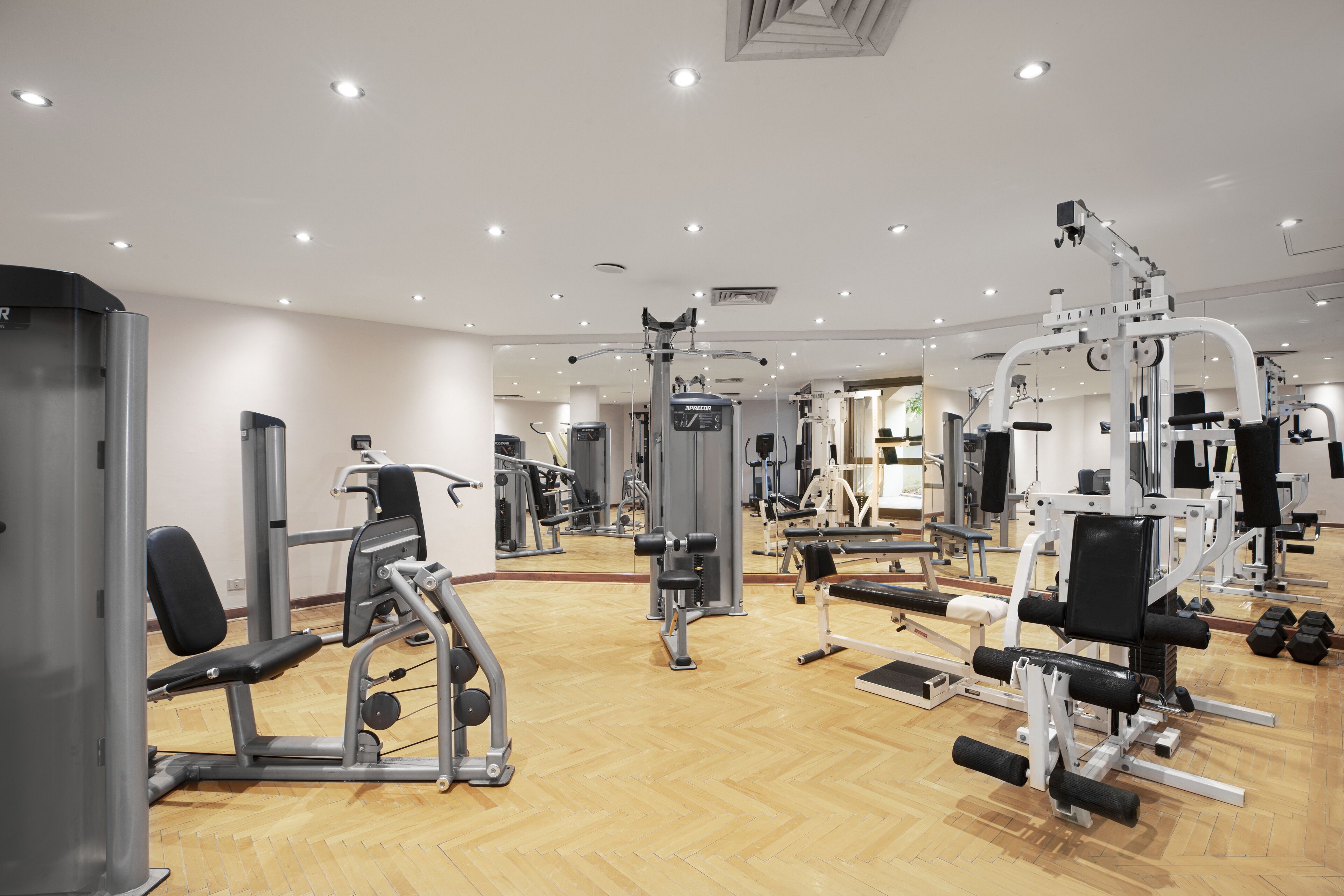 A gym with various exercise machines, wooden flooring, and multiple ceiling lights.