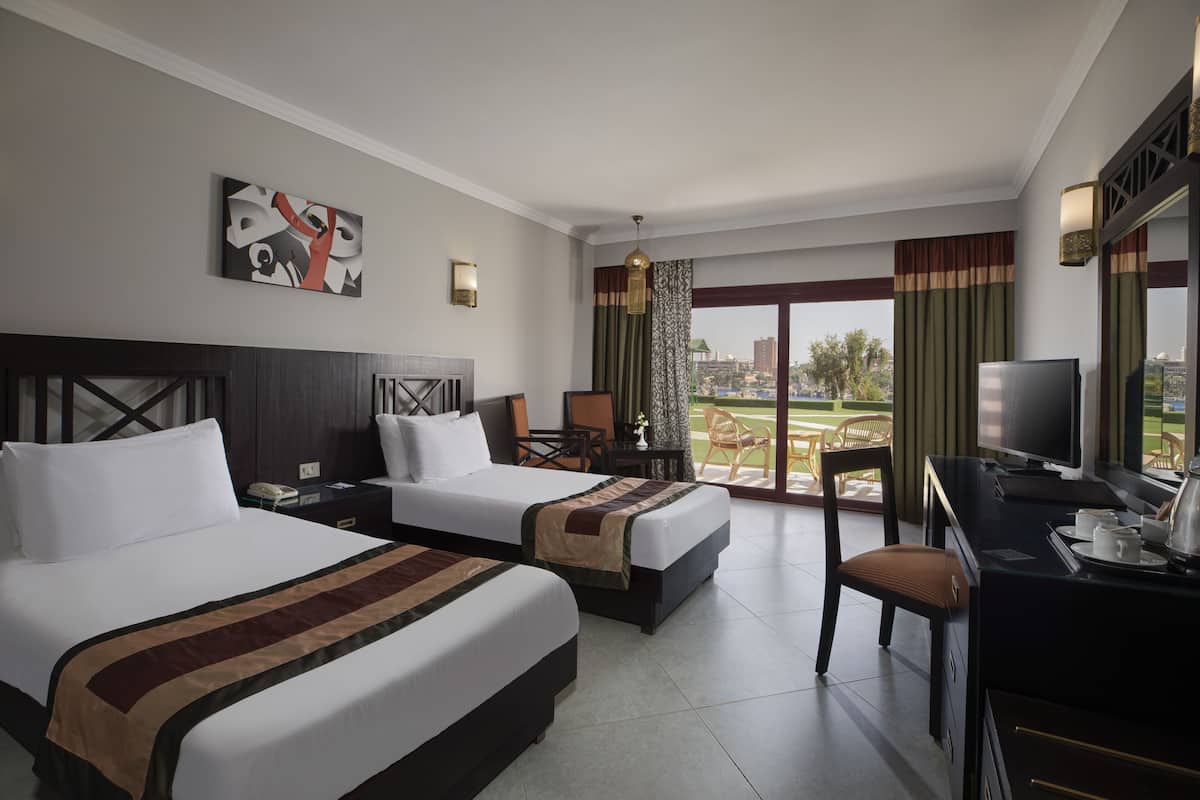 A hotel room with two beds, a desk with a television, and a view of the city.