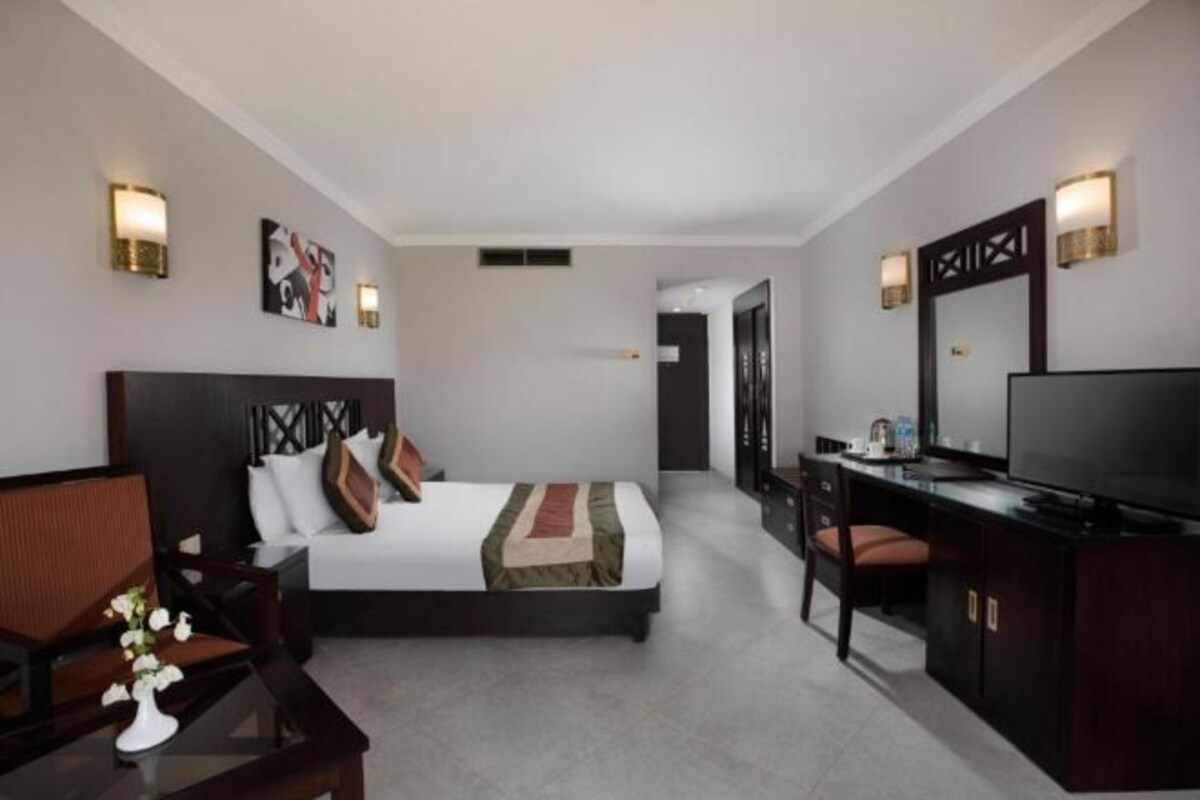 Habitación de hotel con cama, escritorio, televisión y baño visible a través de una puerta abierta.