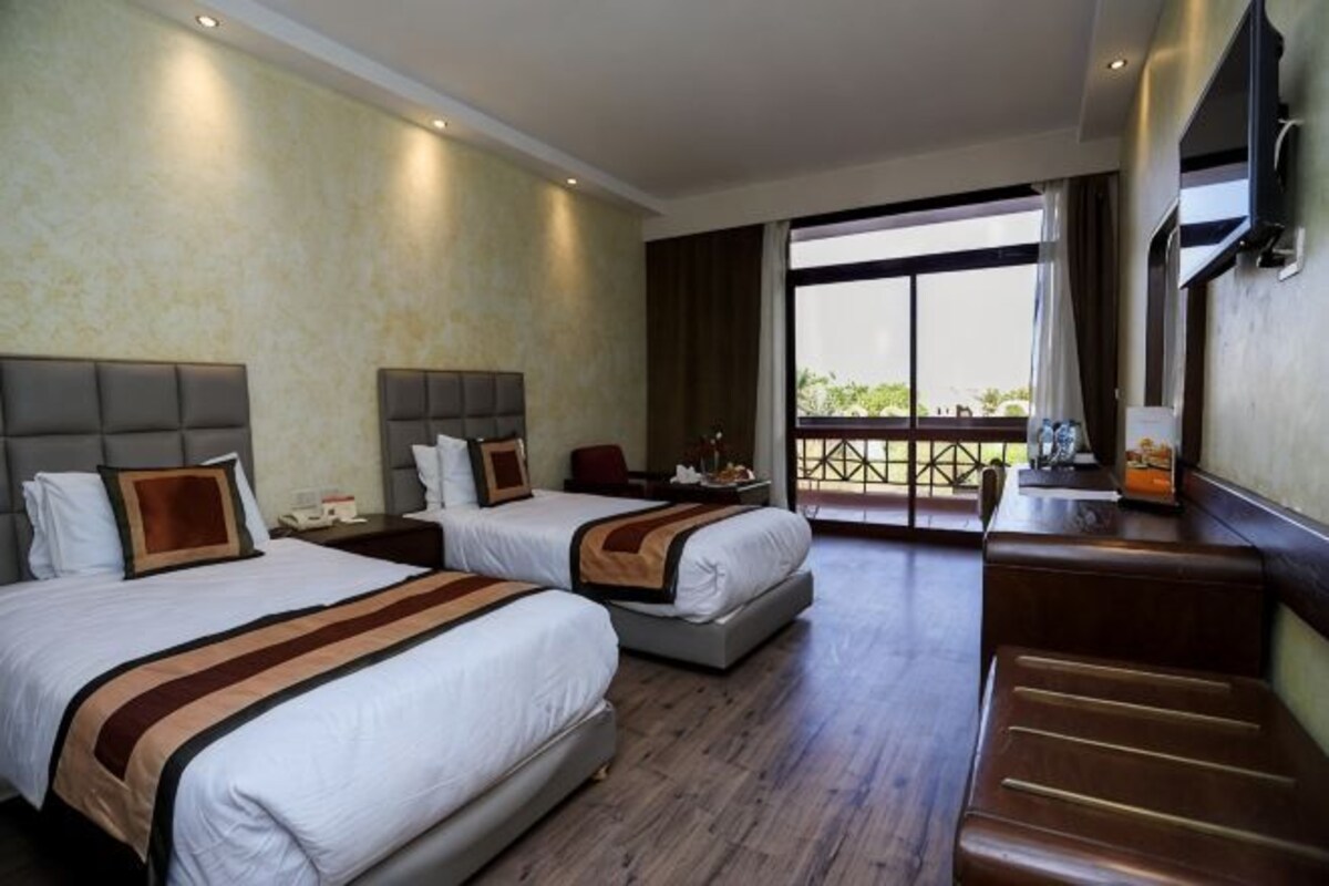 Habitación de hotel con dos camas, zona de estar, balcón y televisión.