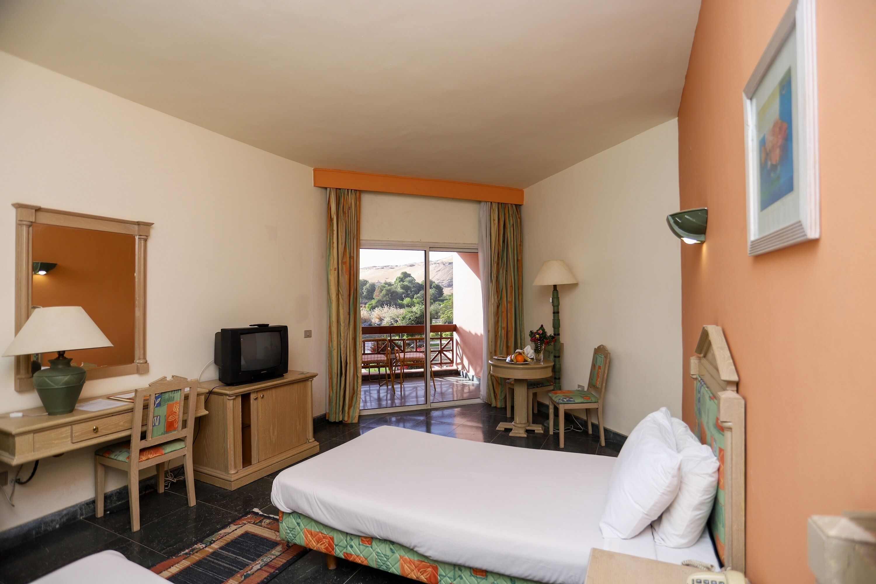 A hotel room with a bed, desk, television, and a balcony with a view.