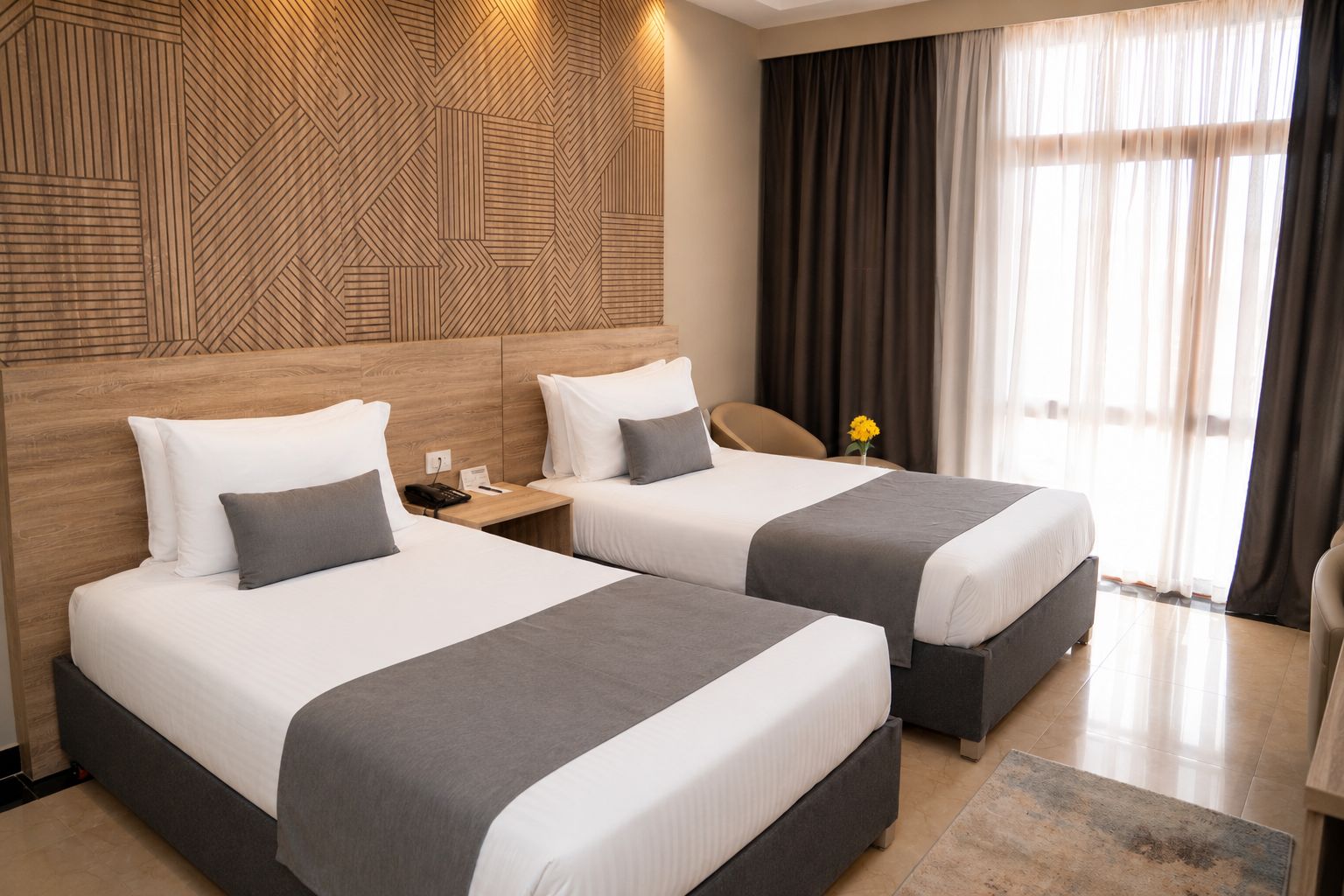 Une chambre d’hôtel avec deux lits, une tête de lit en bois, une table de chevet avec un téléphone et une fenêtre avec des rideaux.