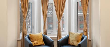 A room with two black leather chairs, a bed, and large windows with curtains.