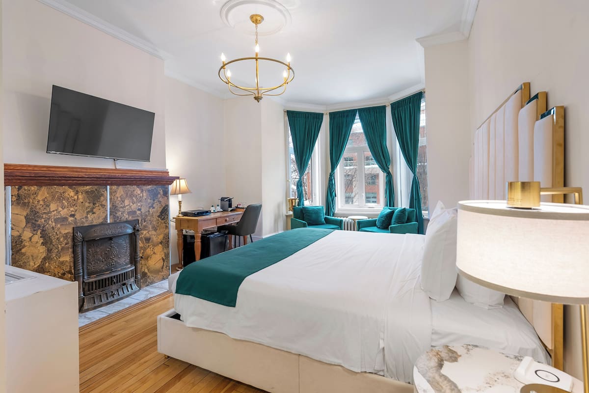 Ein Hotelzimmer mit einem großen Bett, einem Kamin, einem Schreibtisch mit Stuhl, einem an der Wand befestigten Fernseher und einem Fenster mit Vorhängen.
