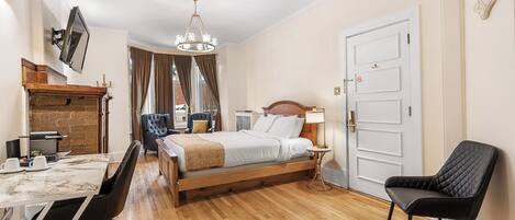 Un dormitorio con cama de madera, una mesa de comedor con sillas, un televisor montado en la pared y una araña.