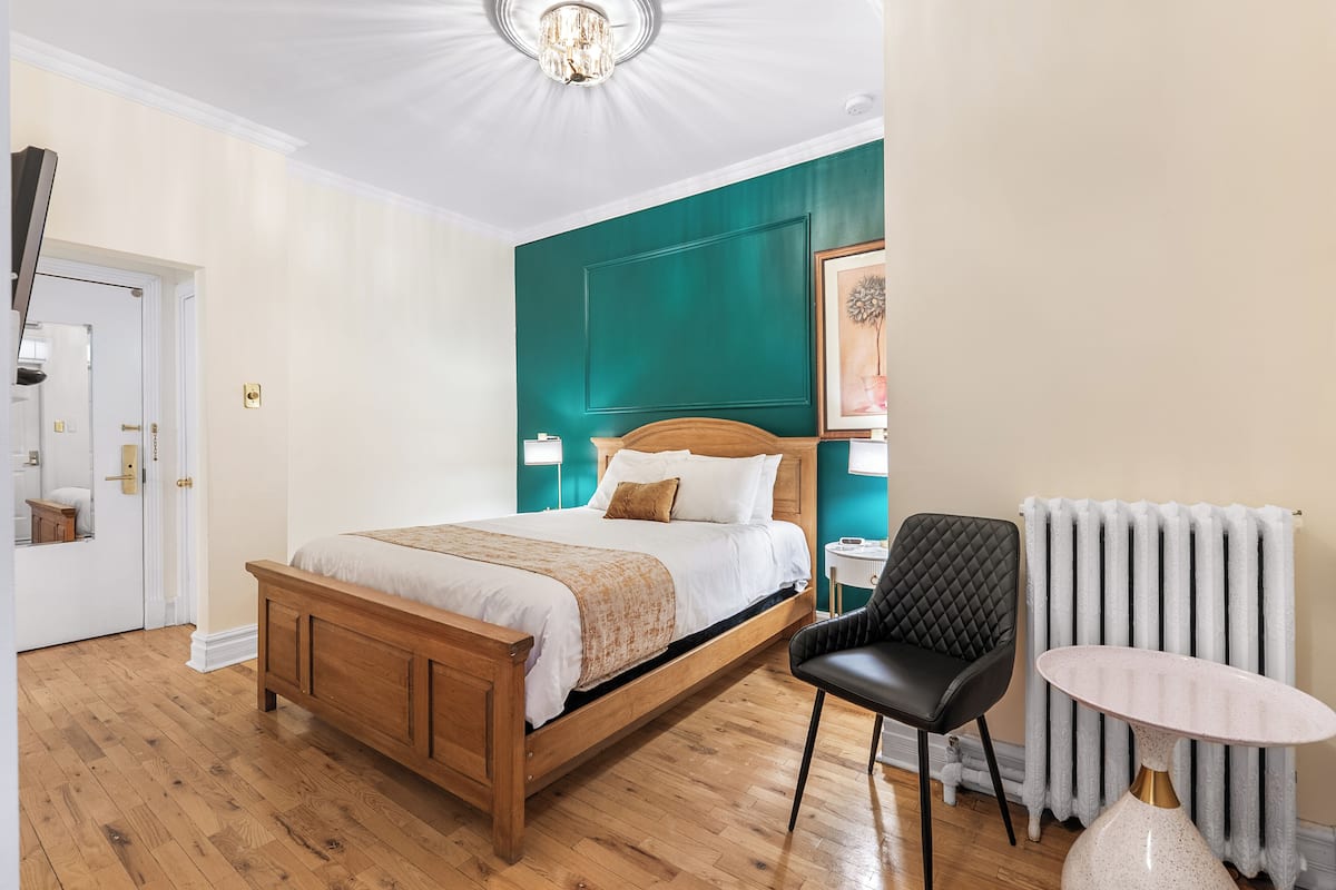 Ein Hotelzimmer mit einem hölzernen Bett, einem schwarzen Stuhl, einem kleinen Tisch und einer Heizung.