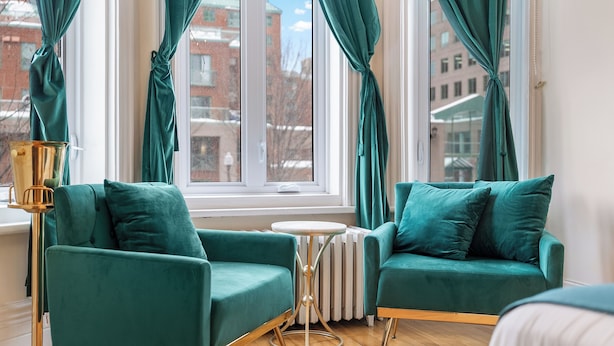 Quarto moderno com duas poltronas azul-esverdeadas, uma mesa redonda pequena e um abajur.