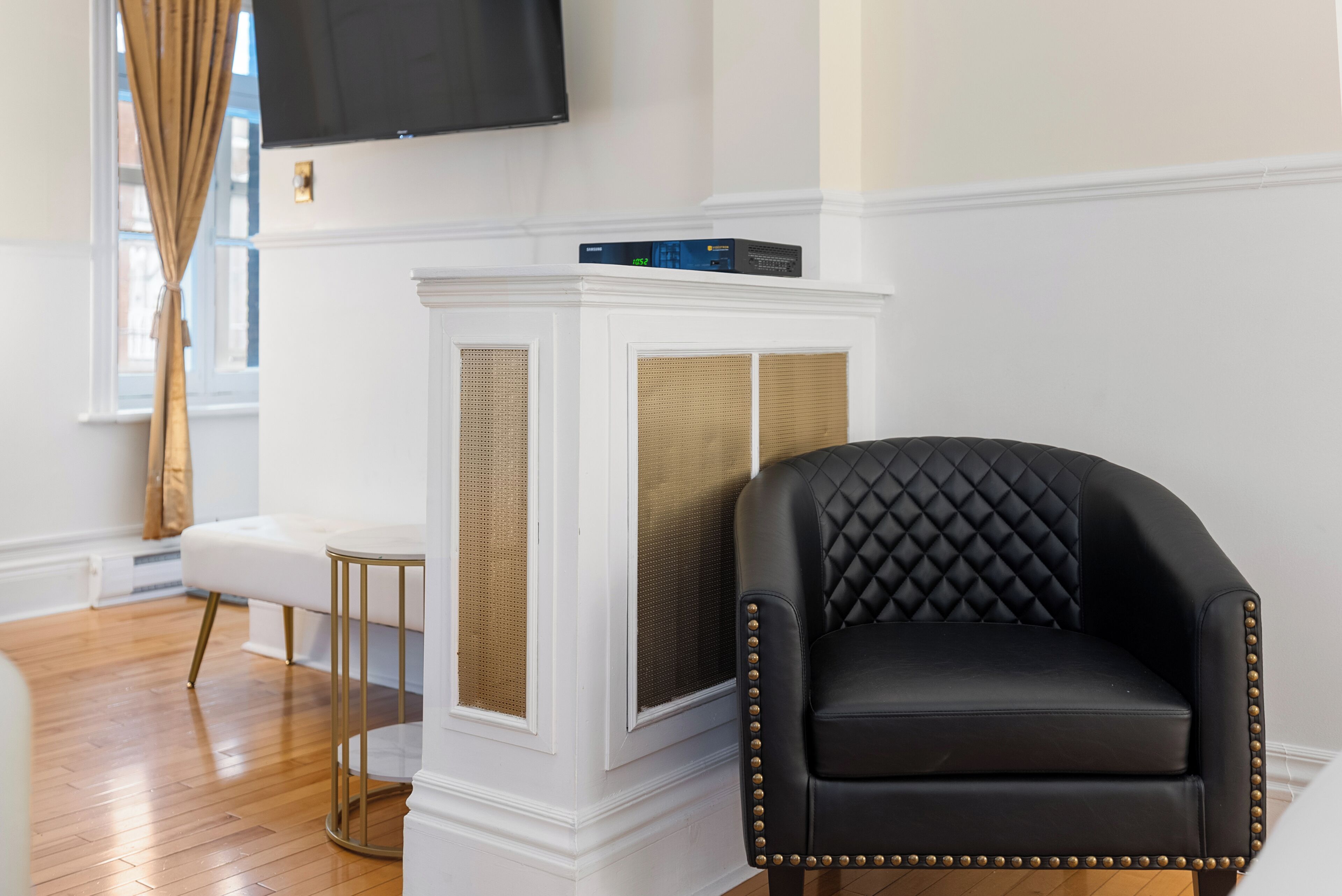 A black leather armchair with gold studs, a white console table with a television, and a wooden floor.