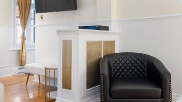 A black leather armchair with gold studs, a white console table with a television, and a wooden floor.