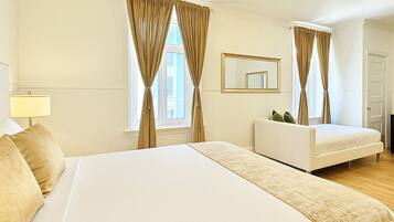 A hotel room with a large bed, a sofa, a chandelier, and a mirror on the wall.
