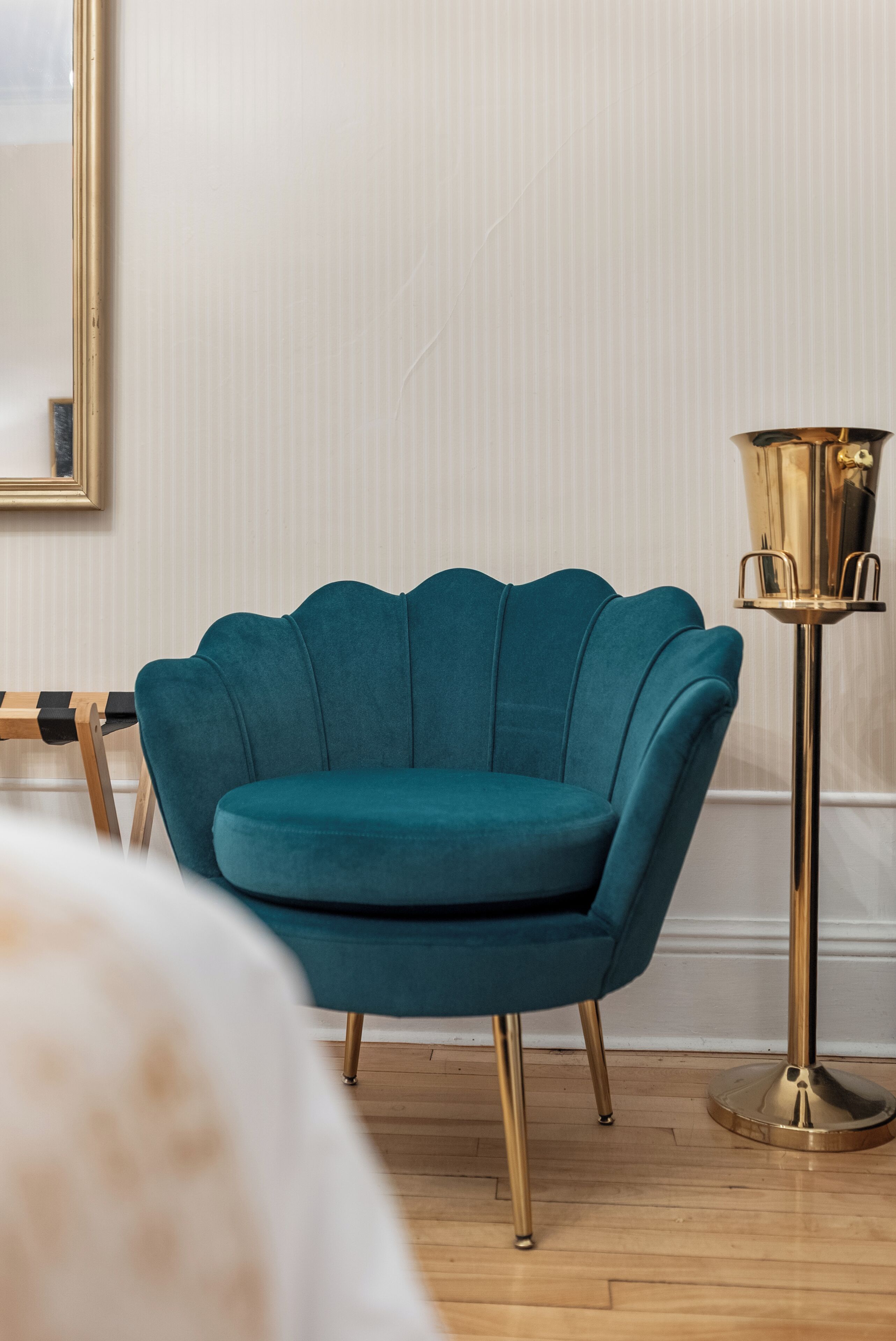 Un sillón color turquesa con patas doradas, una lámpara de pie dorada y un suelo de madera.
