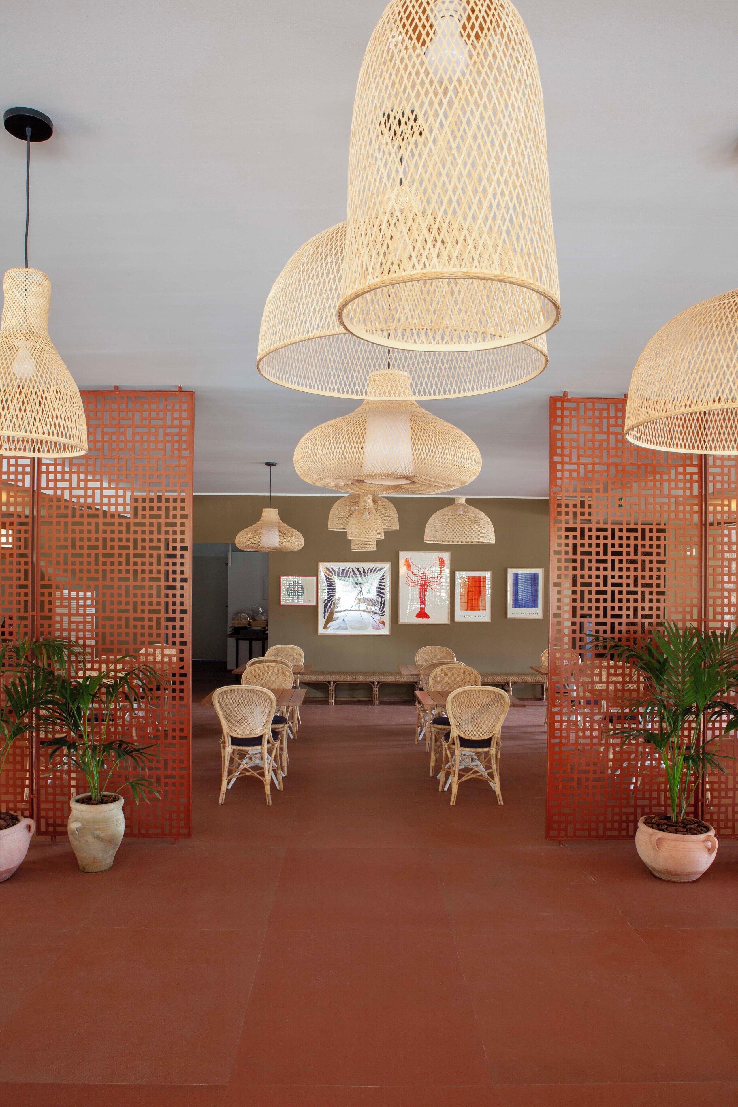 A room with wicker pendant lights, wicker chairs, and potted plants.
