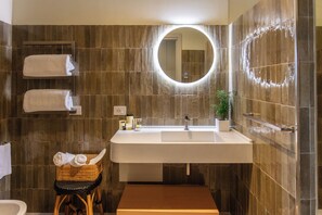 A modern bathroom with a large sink, a round mirror, and a wooden bench.