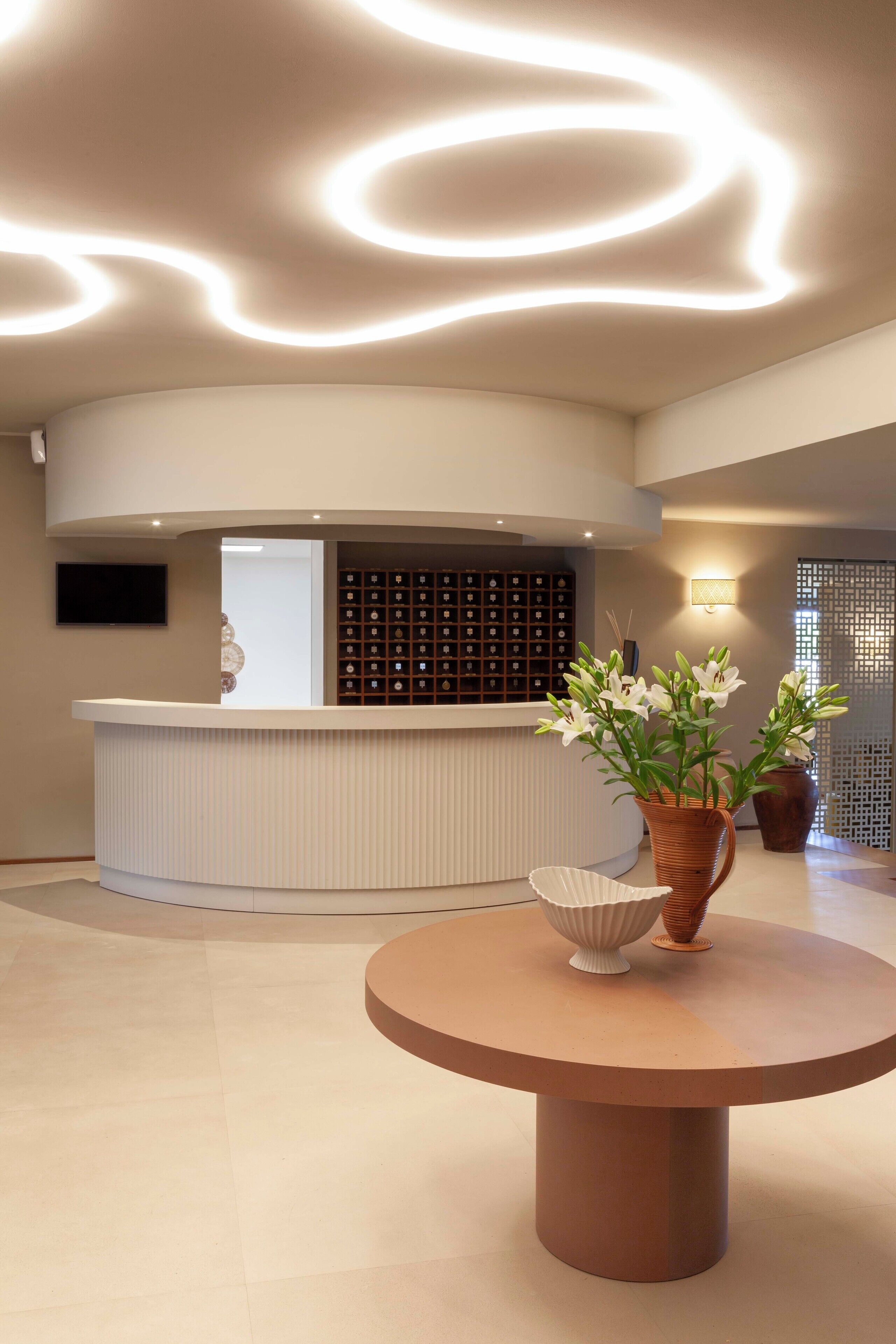 A reception area with a curved counter, a round table with a vase of flowers, and a wall-mounted TV.
