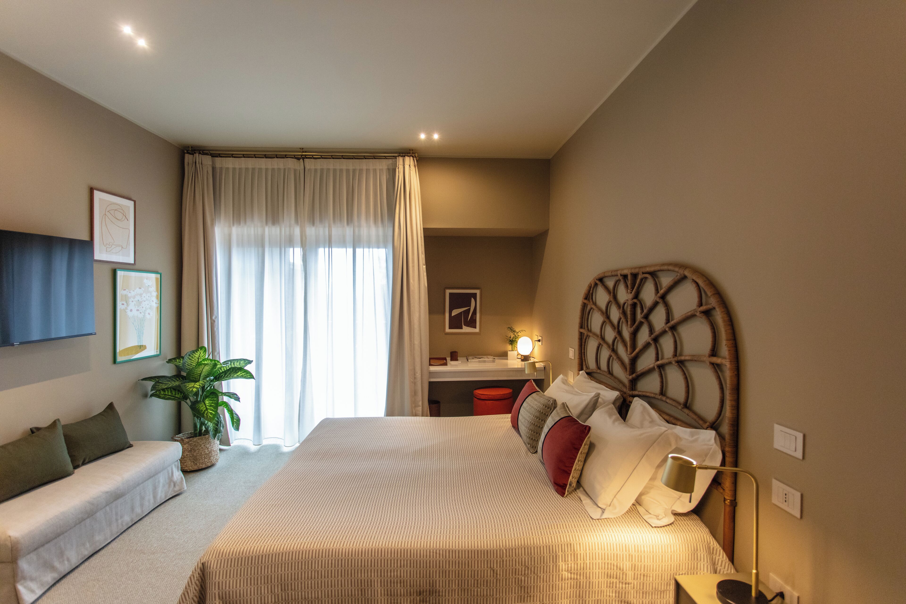 A bedroom with a bed, a desk, a chair, a sofa, and a potted plant.