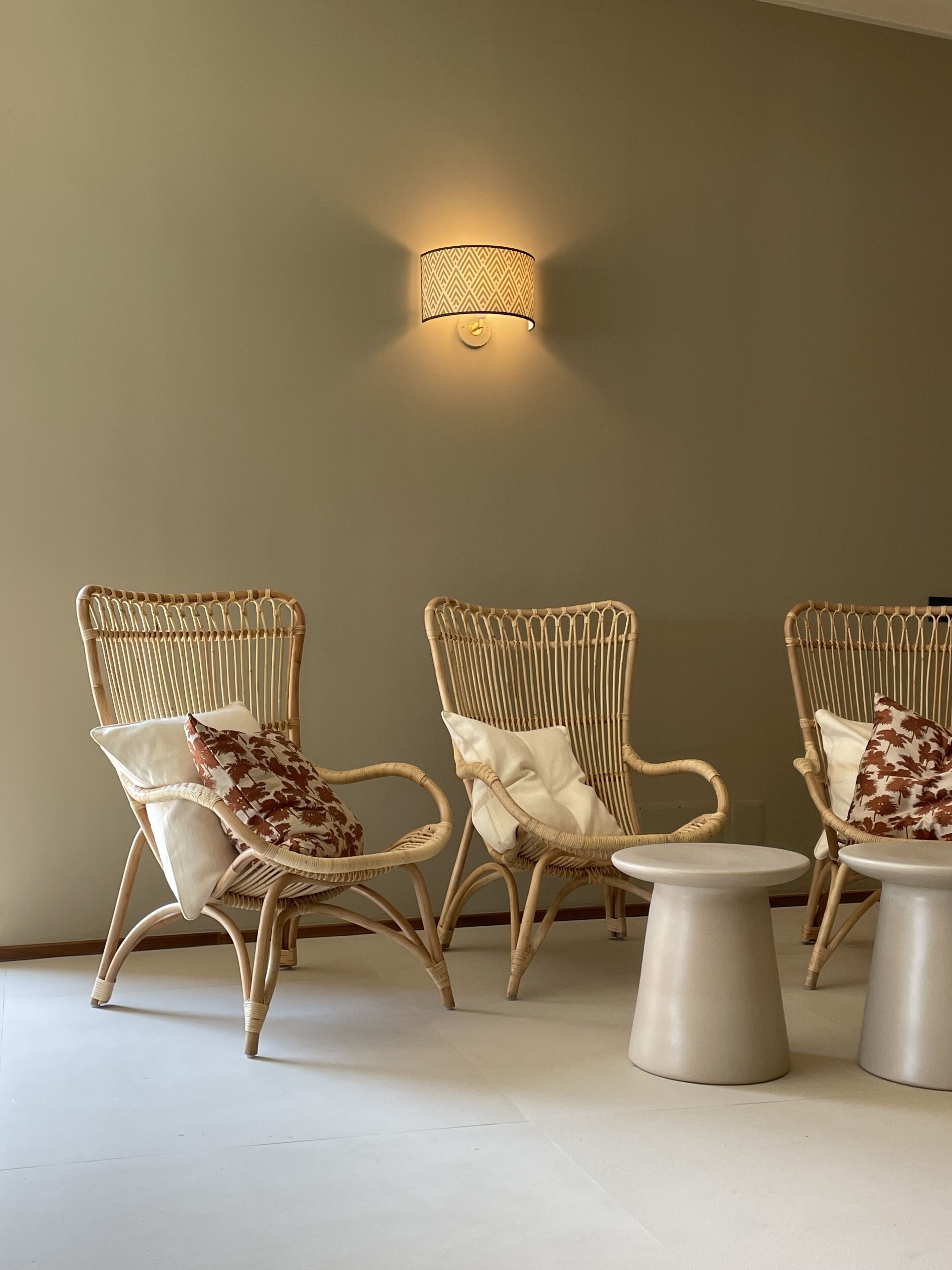 Three wicker chairs with cushions, a wall-mounted light fixture, and two small round tables.