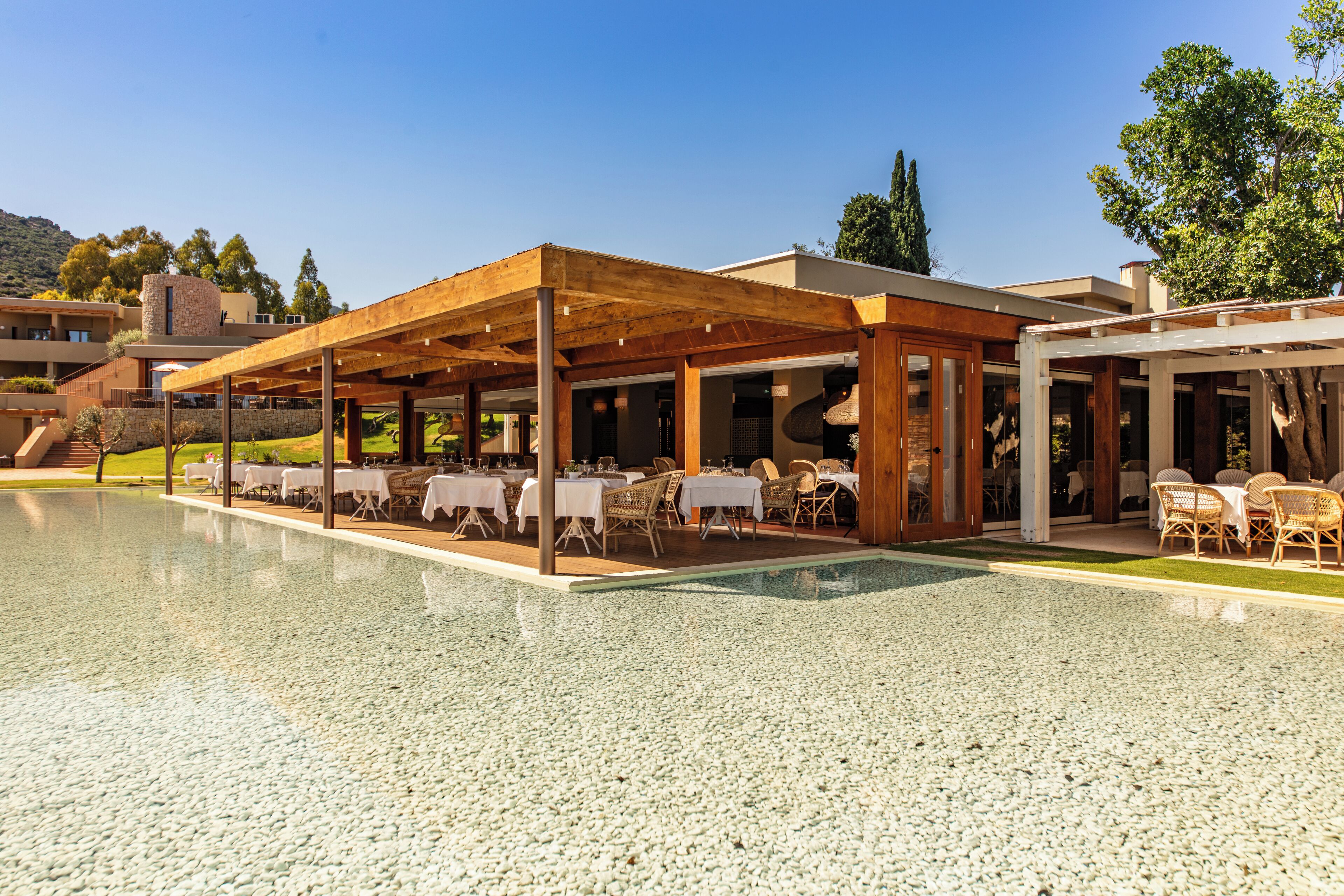 An outdoor pool area with a covered patio, tables, and chairs.