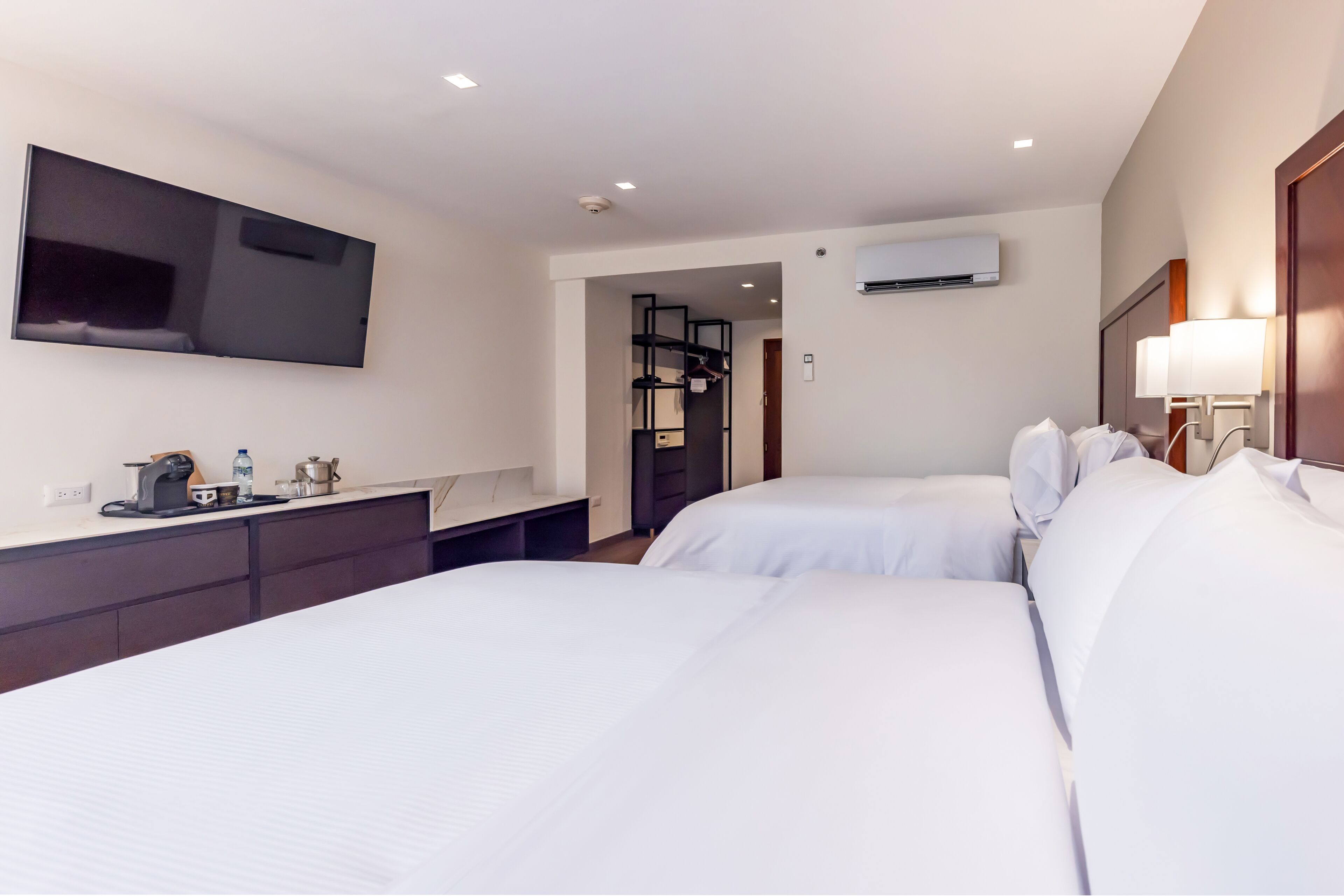 A hotel room with two beds, a flat-screen TV, a desk with a kettle, and a wardrobe.