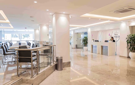 A hotel lobby with a reception desk, seating area, and large windows.