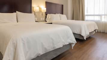 Habitación de hotel con dos camas, cabecero de madera oscura, mesita de noche con lámparas y un ventanal con cortinas.