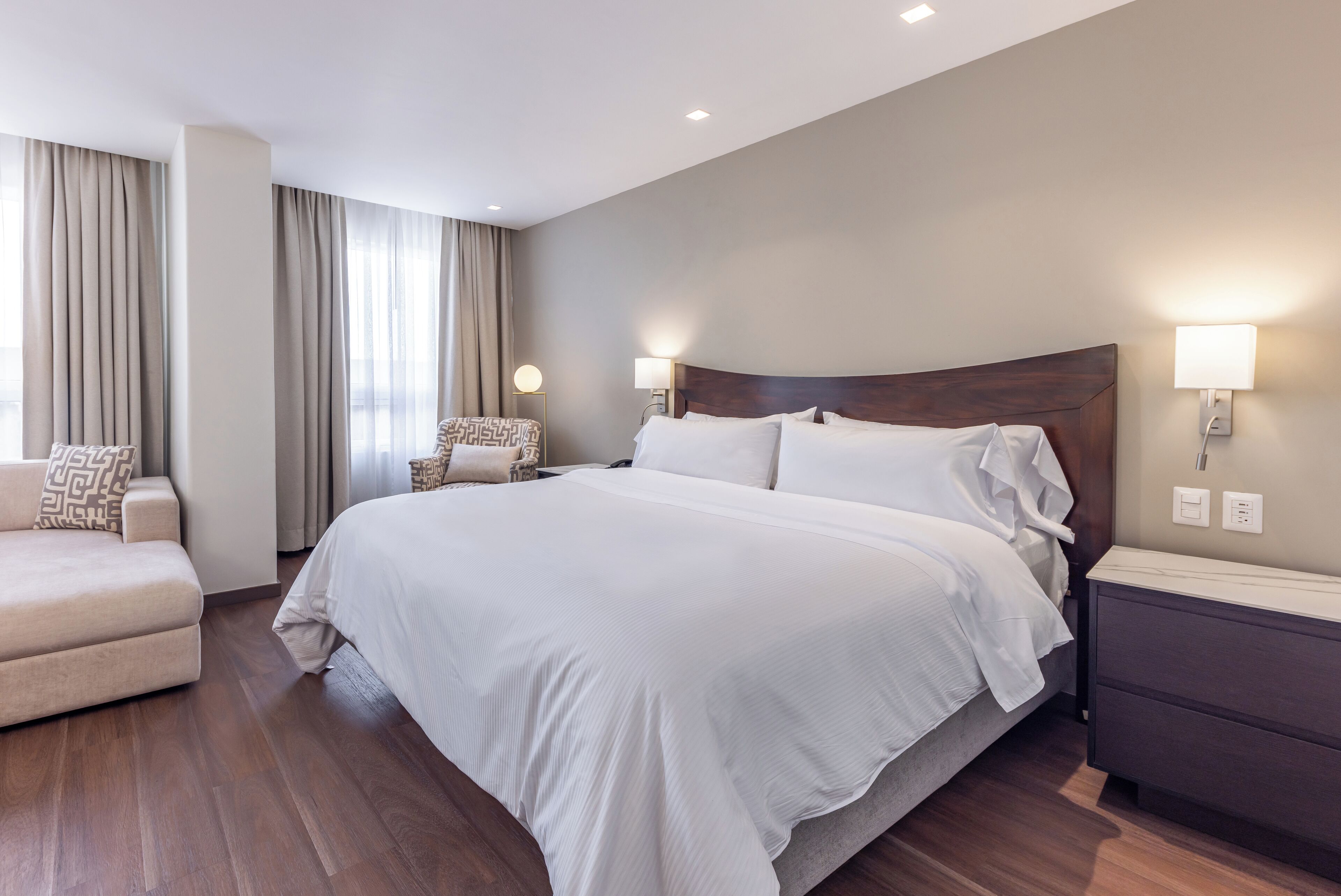Una habitación de hotel moderna con una cama grande, un sofá y una mesita de noche.