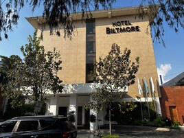 Ein Hotel namens "HOTEL BILTMORE" mit modernem Design, das einen markanten Eingang und einen Parkplatz mit einem Auto und einem Elektroroller zeigt.