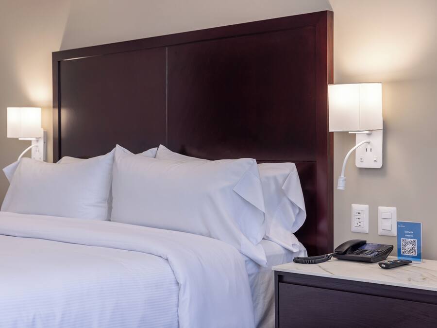 Una camera d'albergo con un letto grande, due lampade sui comodini, un telefono e un codice QR apposto sul tavolino.