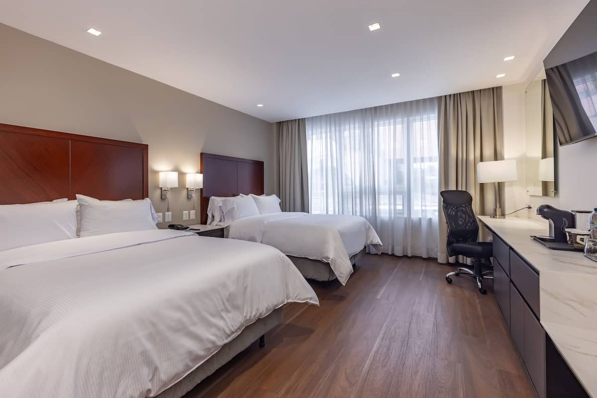 Une chambre d’hôtel avec deux lits, un bureau, une chaise et une grande fenêtre avec des rideaux.