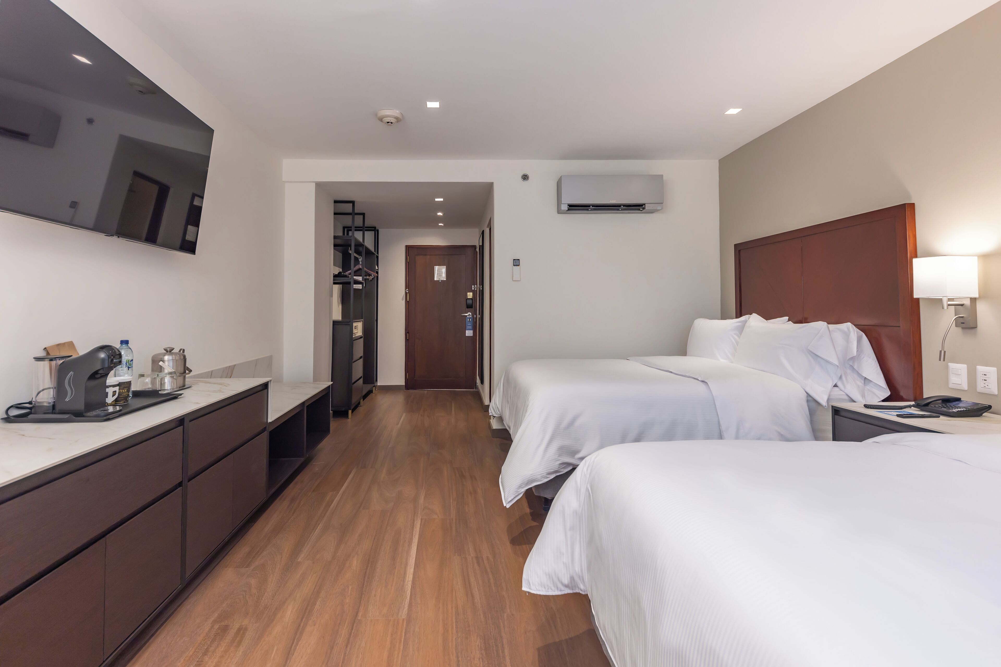 Ein Hotelzimmer mit zwei Betten, einer Küchenzeile, einem großen Spiegel und einer Klimaanlage.