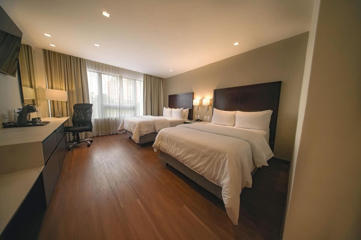 Une chambre d’hôtel avec deux lits, un bureau, une chaise et une grande fenêtre avec des rideaux.