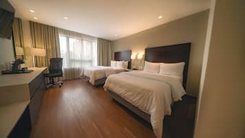 Habitación de hotel con dos camas, un escritorio, una silla y un amplio ventanal con cortinas.