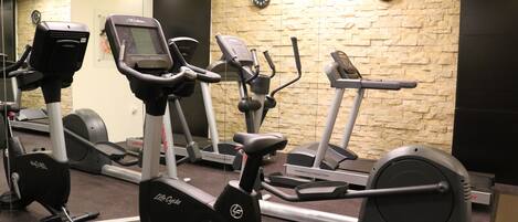 Un gimnasio con varias máquinas de cardio, una pared de piedra y relojes en la pared.