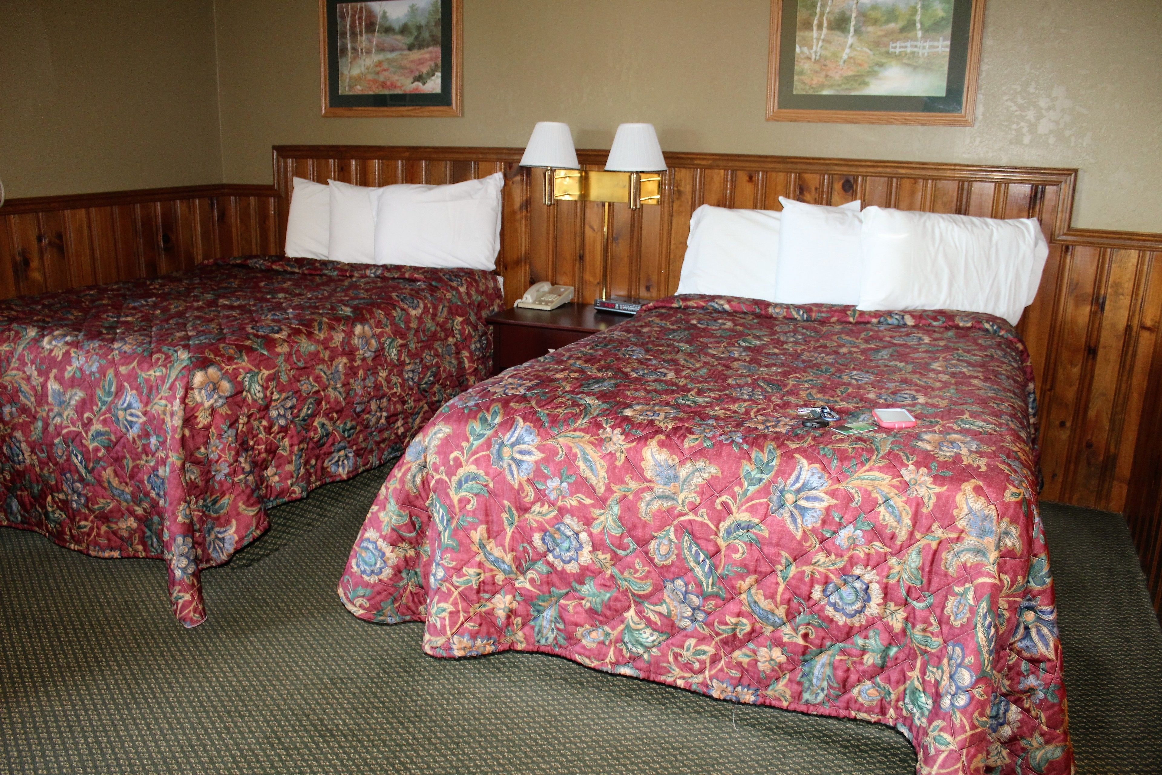 A hotel room with two beds, each with a floral bedspread and white pillows. There are two wall-mounted lamps and a telephone on a nightstand.