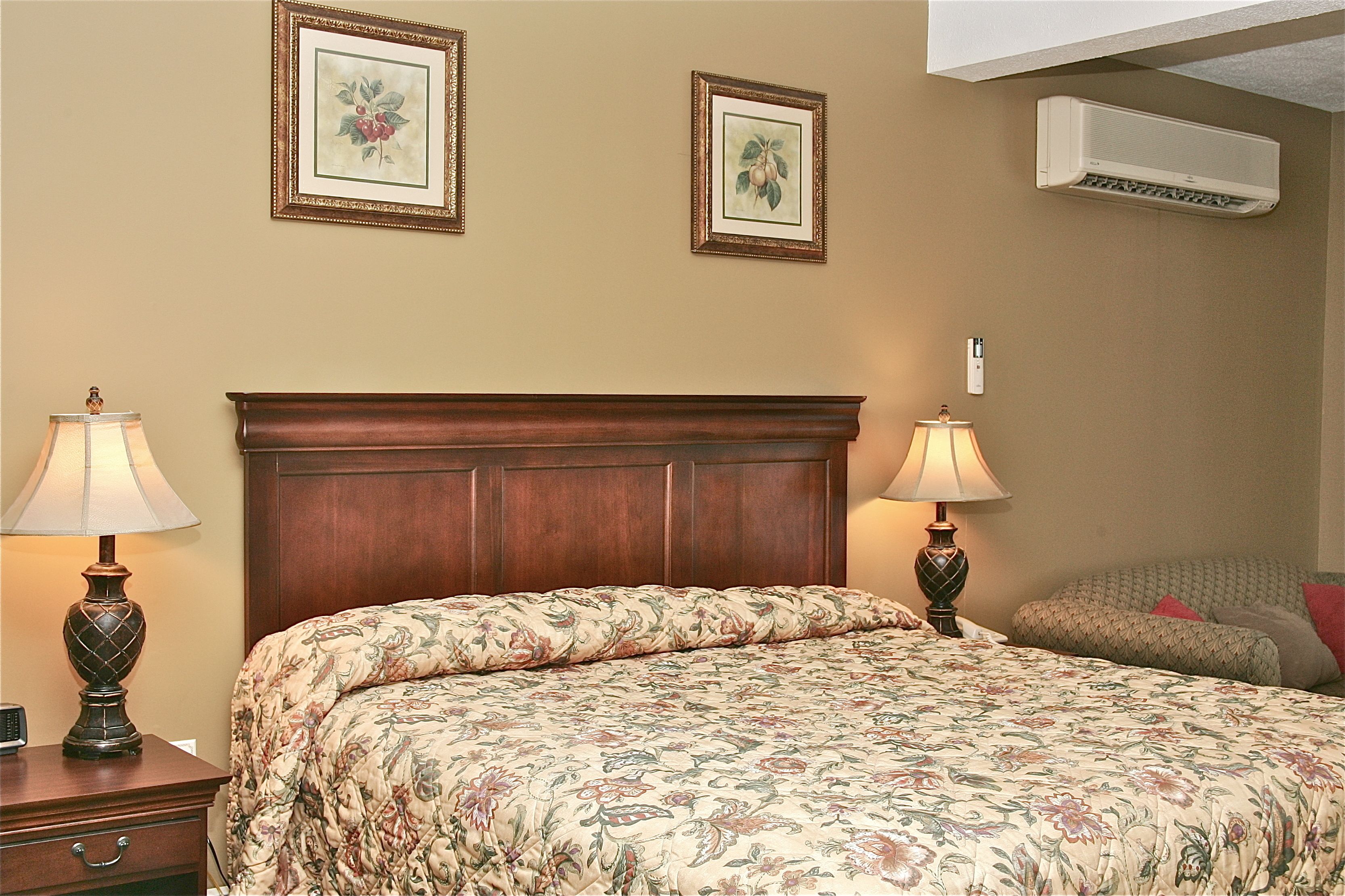 A neatly made bed with floral bedding, two bedside lamps, a wooden headboard, and two framed floral pictures on the wall.