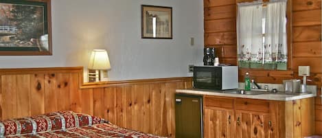 Ein Zimmer mit einem Bett, einer kleinen Küchenzeile, einem Fenster mit Vorhängen und Holzwänden.