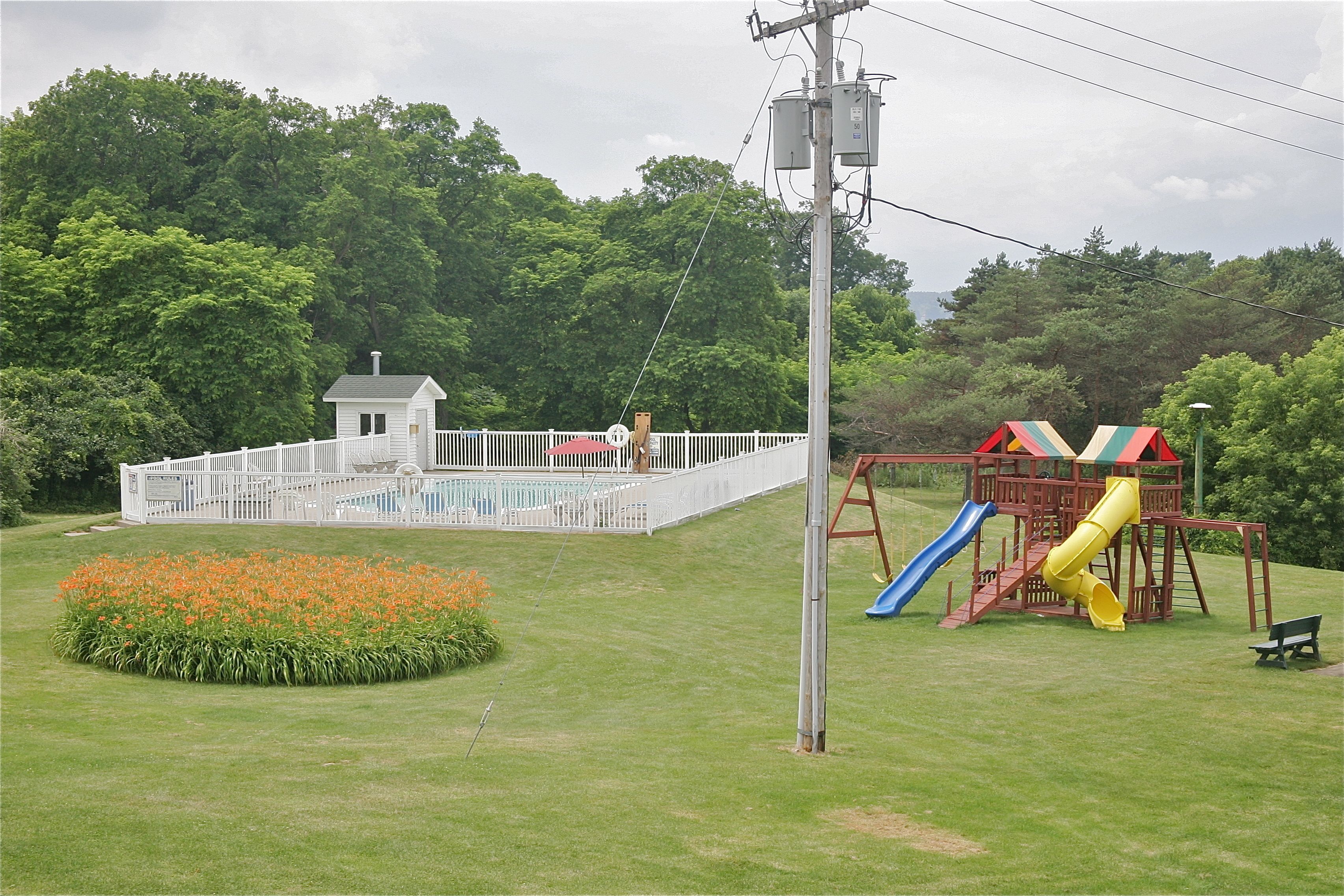 A fenced pool area with a small house, a playground with slides, and a bench.