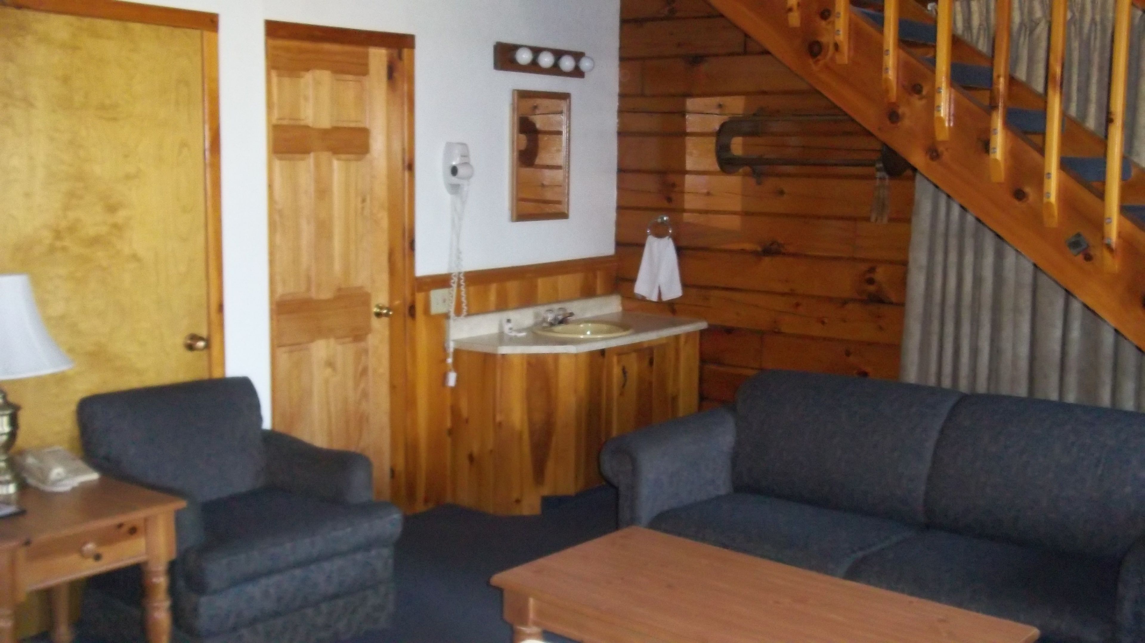 A cozy room with a wooden staircase, a sink, and two sofas.