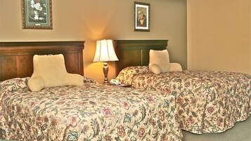 A hotel room with two beds, a nightstand, a lamp, and two framed floral pictures on the wall.
