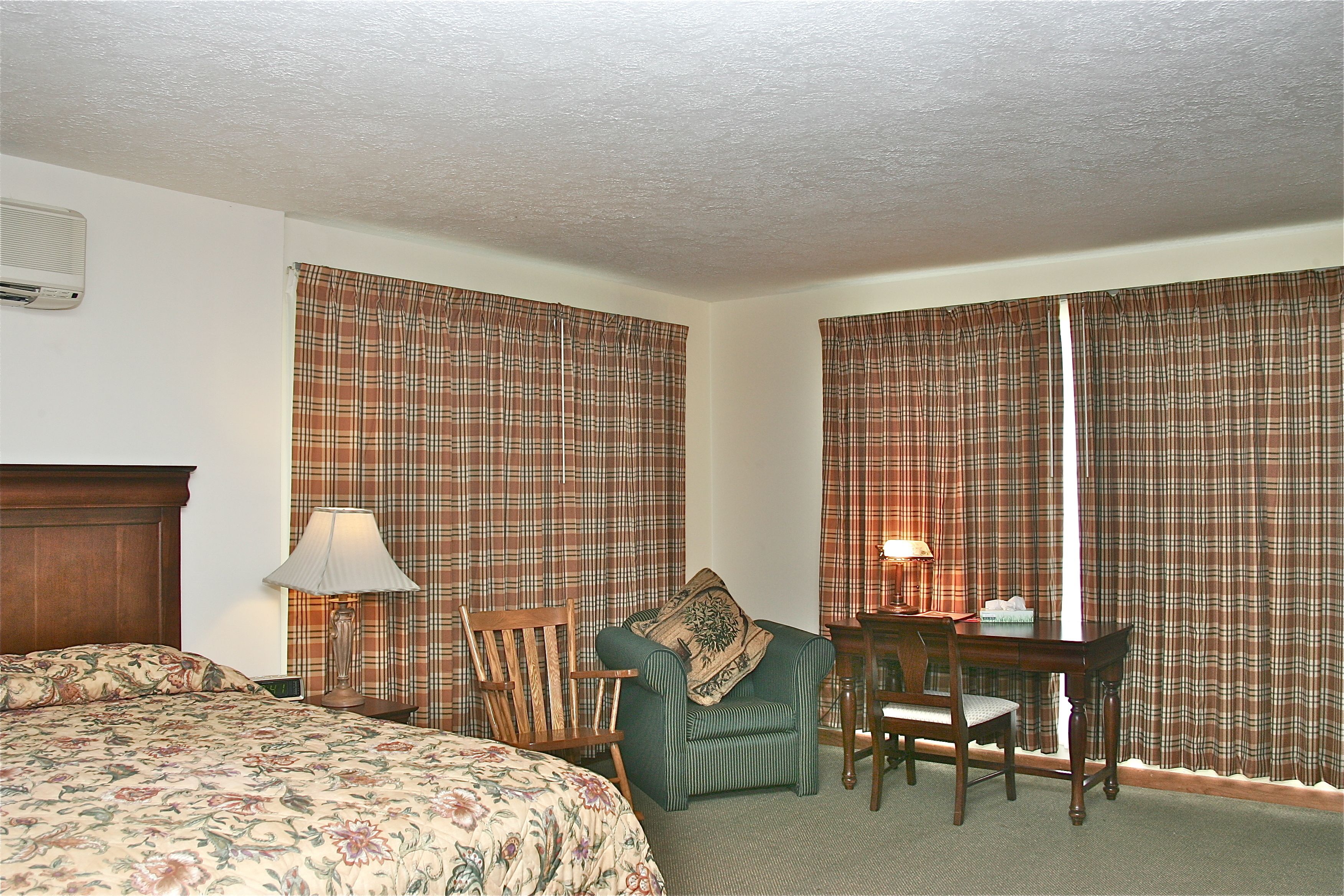 A hotel room with a bed, a chair, a desk, and curtains.