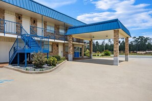 A two-story building with a covered parking area and a blue staircase. - Rodeway Inn Baxley (Baxley)