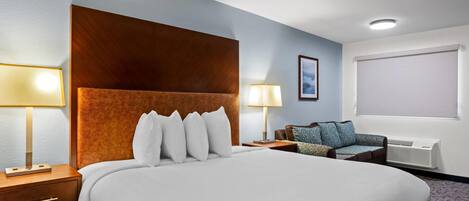 Una habitación de hotel con una cama grande, dos mesitas de noche, un sofá, una ventana con persianas y un aire acondicionado instalado en la pared.