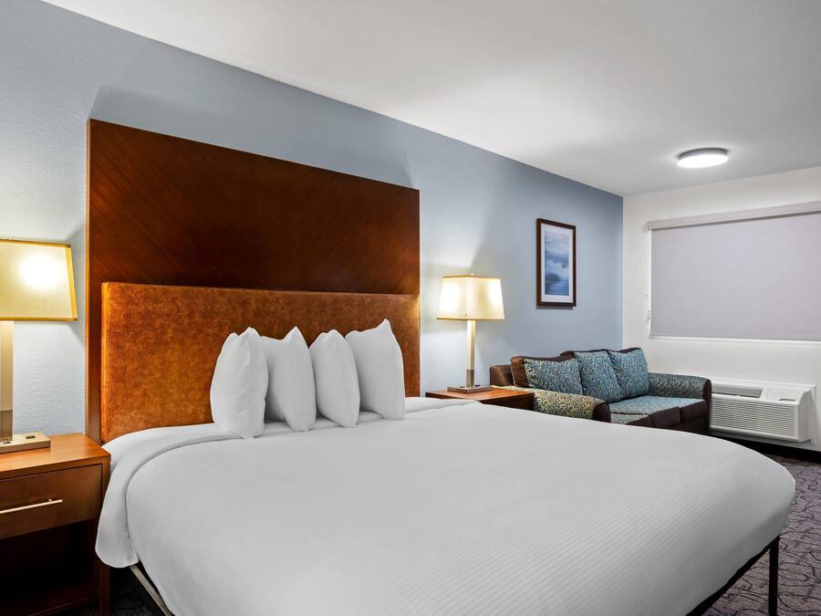 Ein Hotelzimmer mit einem großen Bett, zwei Nachttischen, einem Sofa, einem Fenster mit Jalousien und einer Wand-Klimaanlage.