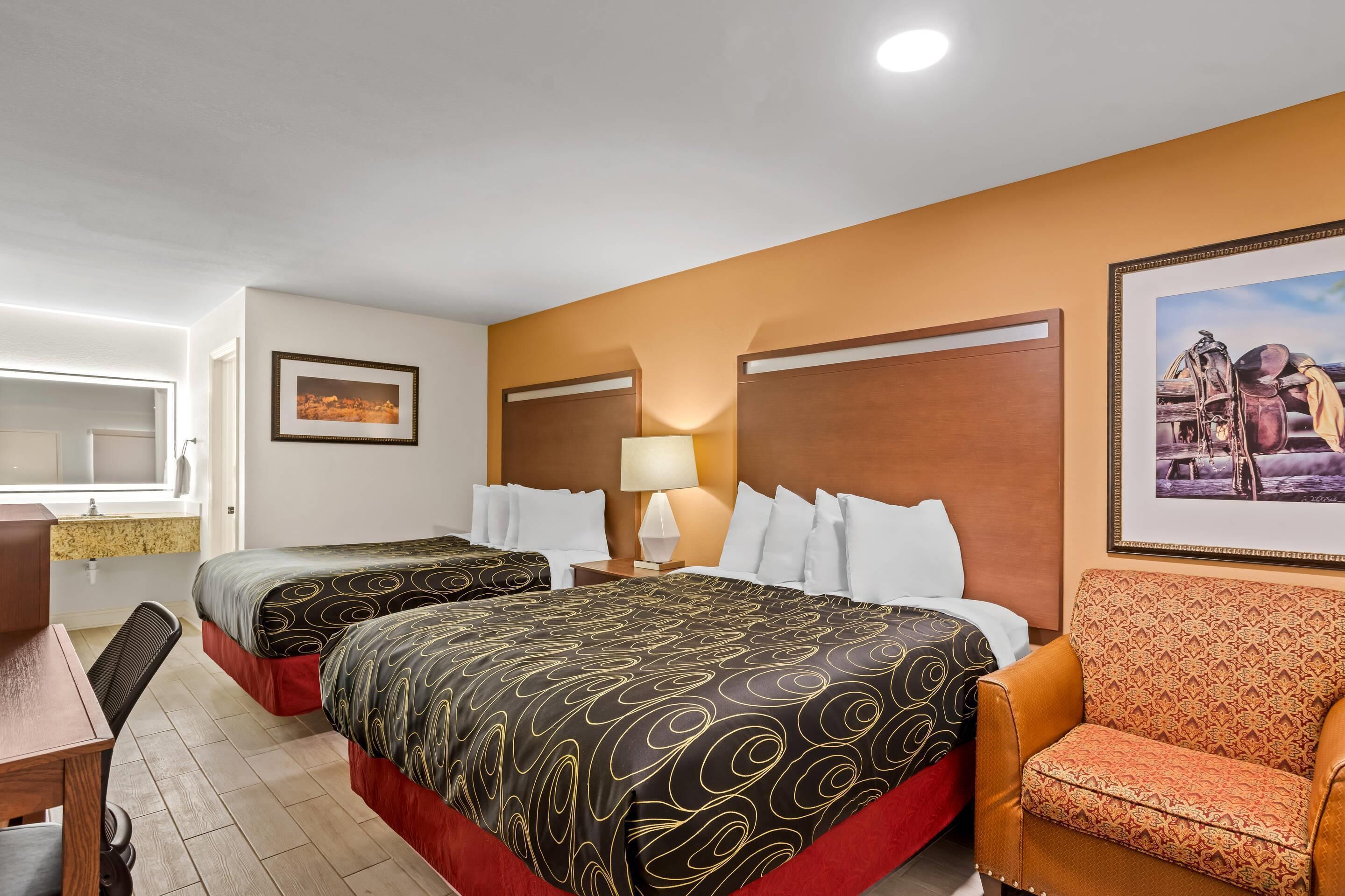 A hotel room with two beds, a desk, a chair, and a painting on the wall.